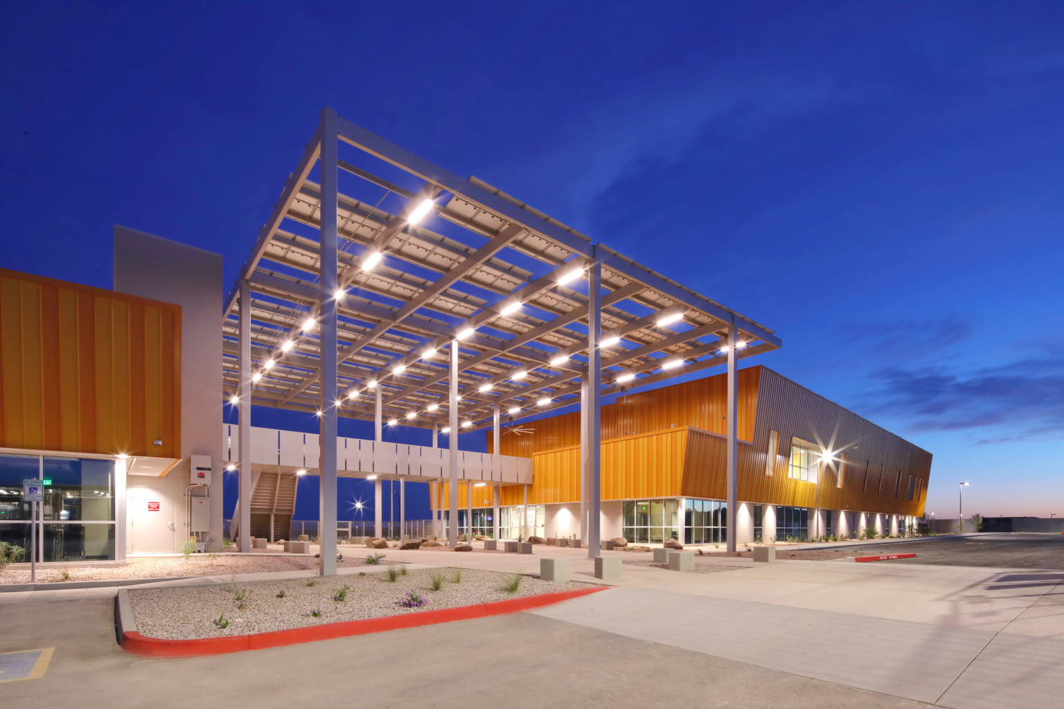 West-MEC school entrance with illuminated canopy with cutouts over wide walkway and elevated path connecting yellow buildings