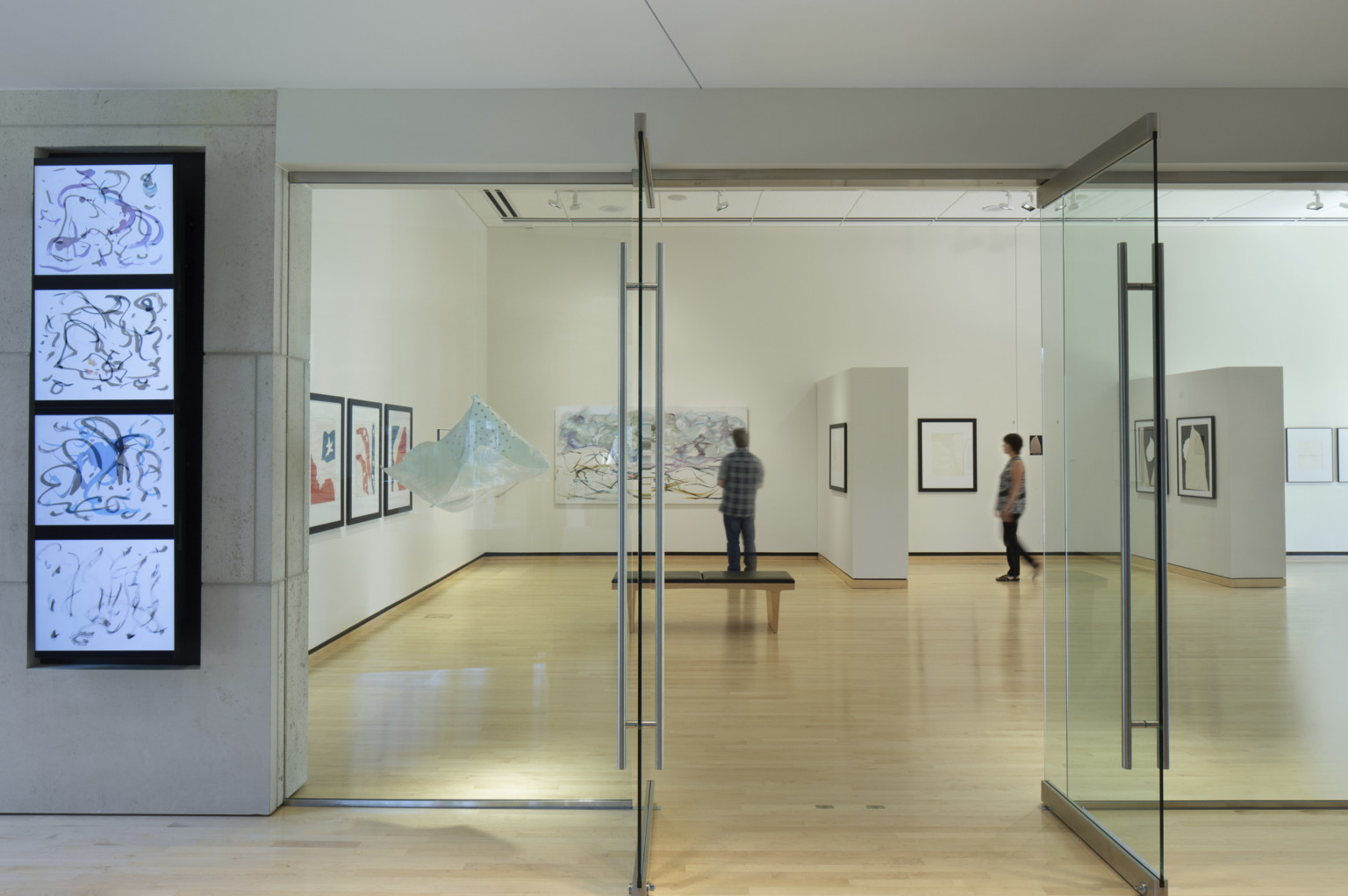 Washburn University Rita Blitt Gallery Addition. Glass doors, interactive screen, left, warm wood floors, and white walls