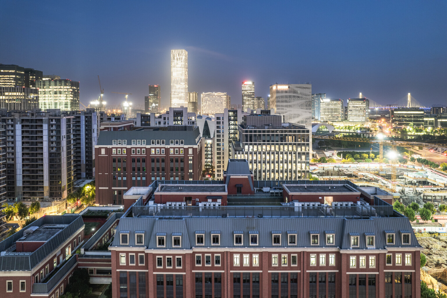 multistory brick building with taller brick and glass midrise towers illuminated at night in a city skyline