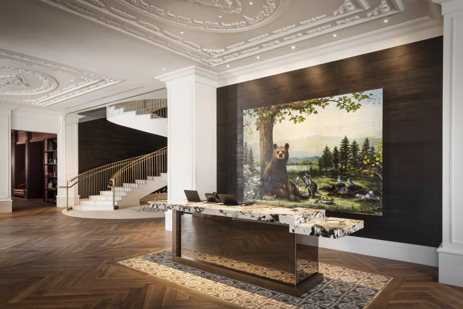Reception desk with white and black marble counter in white lobby in front of recessed wood wall with painting of a bear