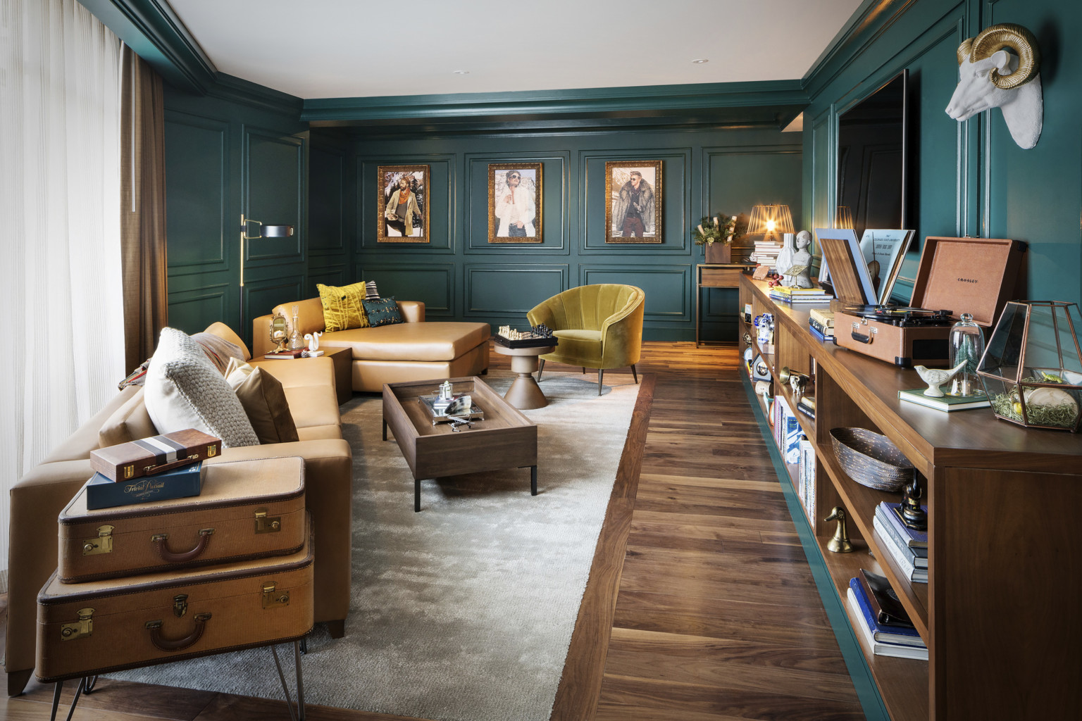 Sitting room with dark green molded walls. Light brown leather couch and yellow velvet chair with wood coffee table and shelf