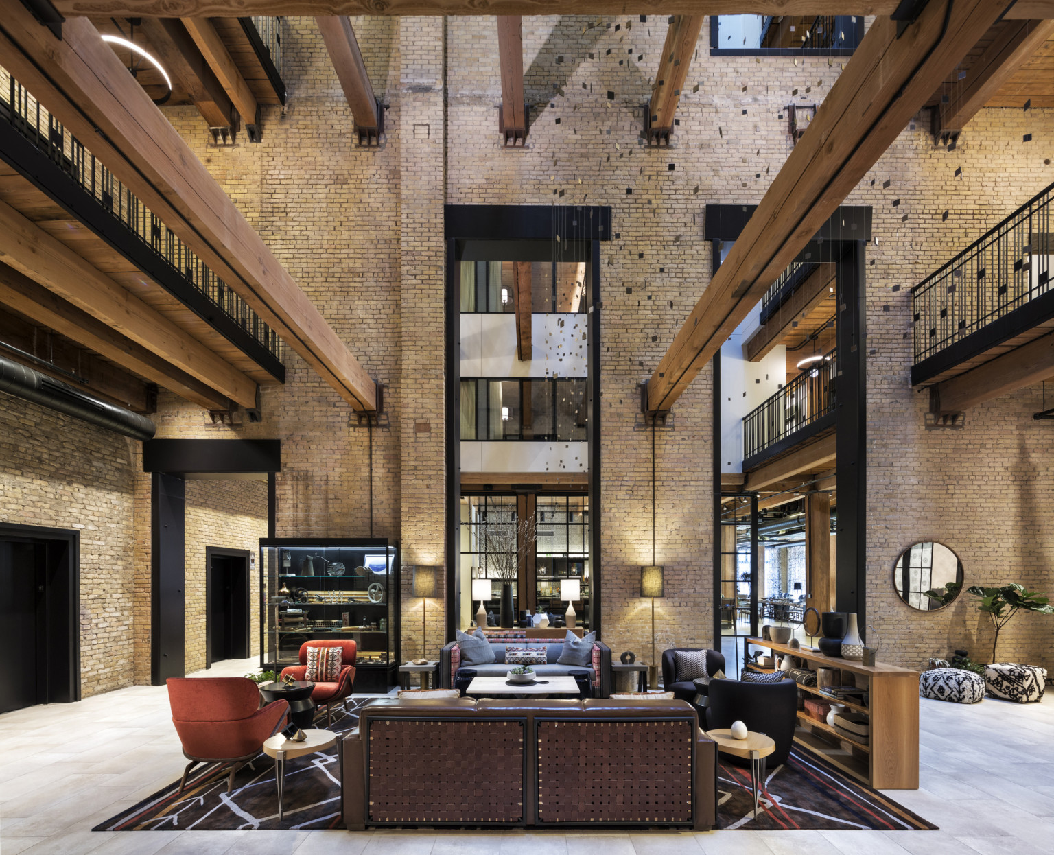 Interior atrium with exposed brick. Seating area at center and wood beams overhead. 2 walkways on sides above with metal rail