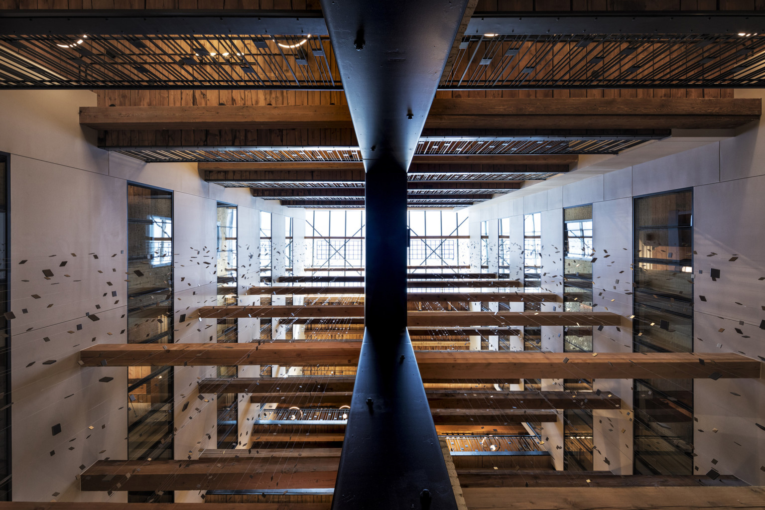 View of multistory atrium from above with walkways at each levels and wood beams between. Strung squares hang from grid above