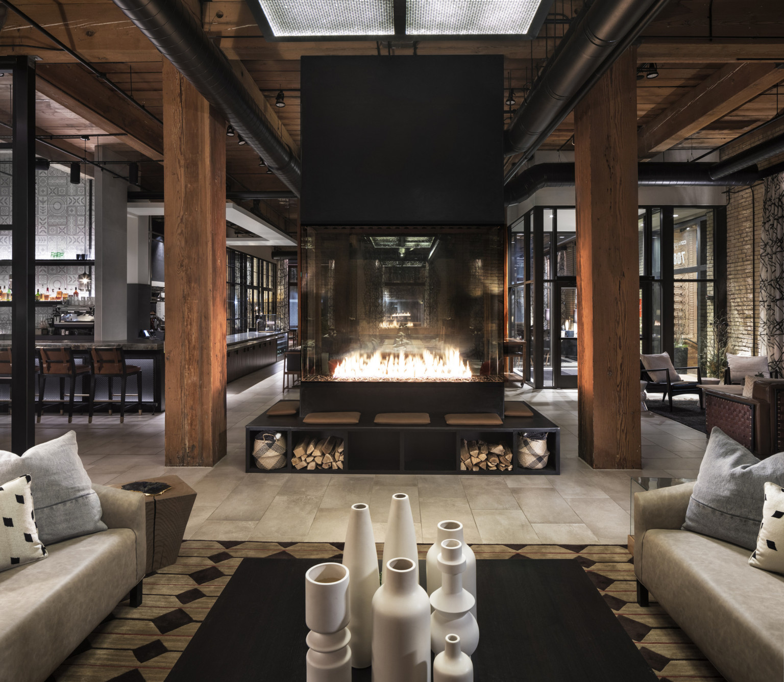 Fireplace elevated on black bench with under seat storage between wood pillars in bar with floor to ceiling windows