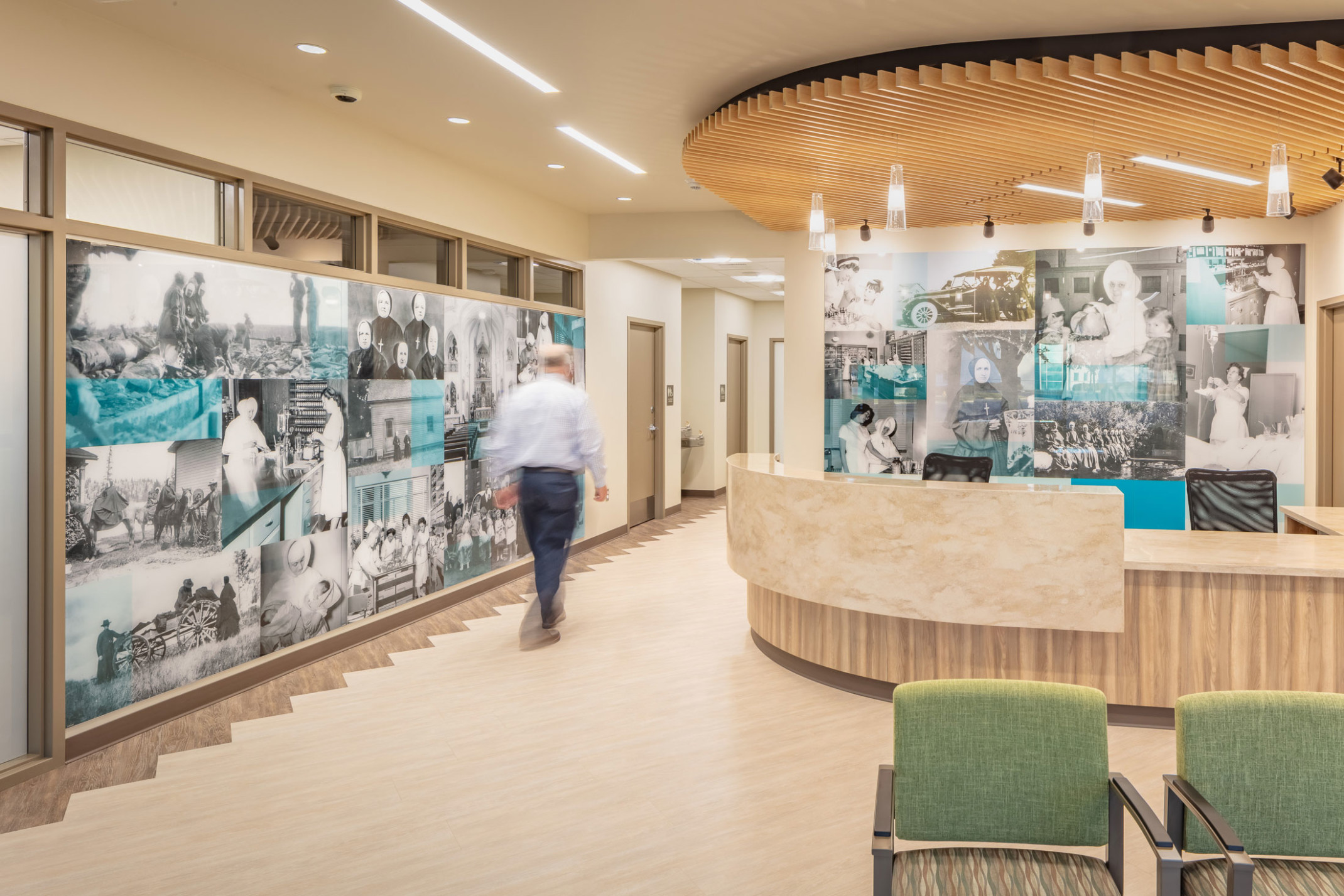 man walking through inside of building with desk area and photos on walls and wood accents