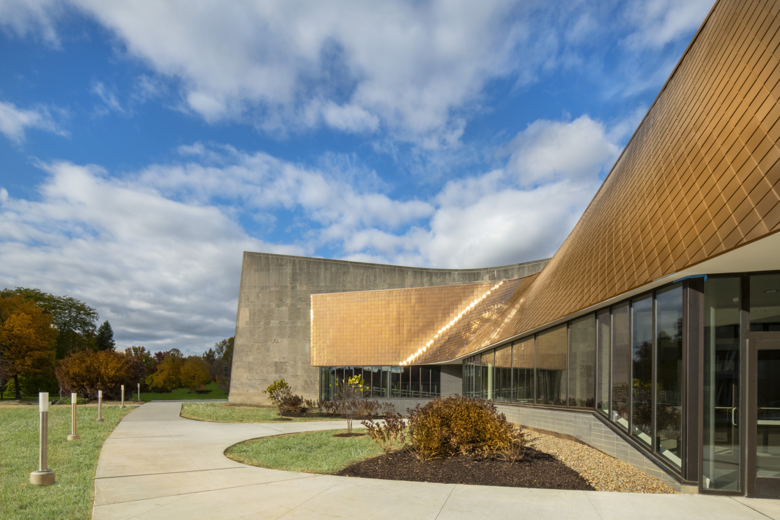 Copper tiled overhang of windowed entryway sits in front of stone building wall, mirroring some of the buildings curves