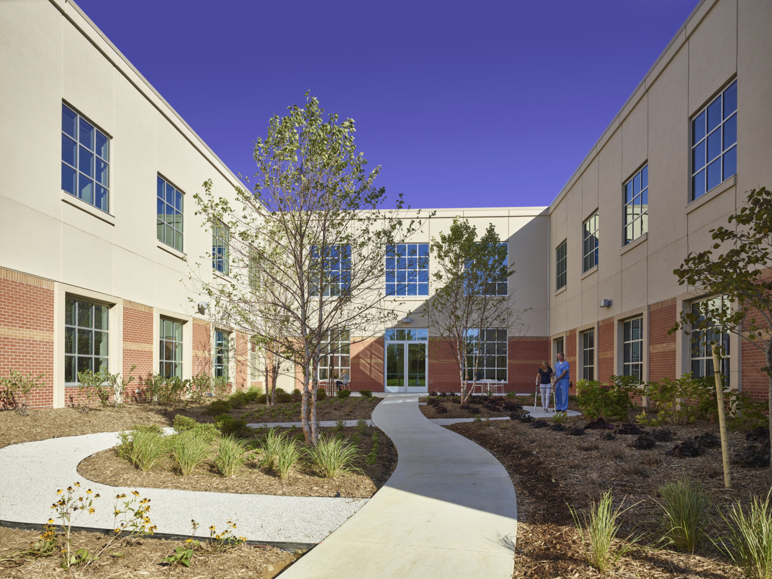 Courtyard with paths surrounded by two story building. Walls have brick first floor and stone second, both lined with windows