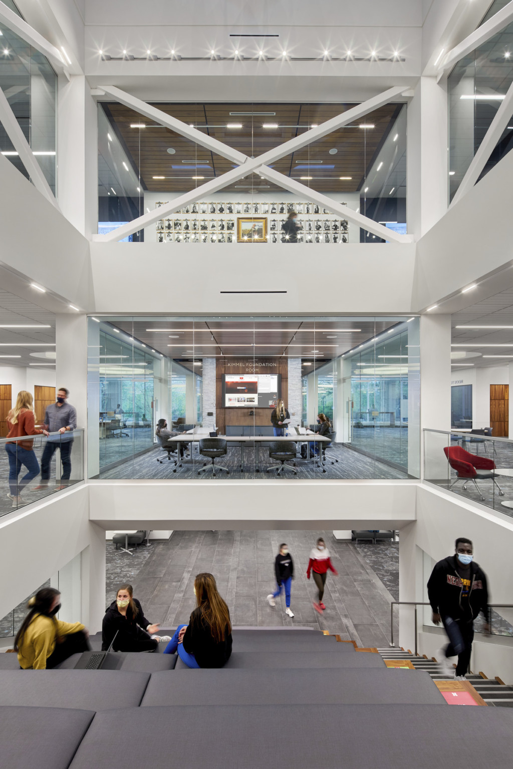 Triple height view with learning spaces on either side of a glass walled conference room with U shaped table facing screen