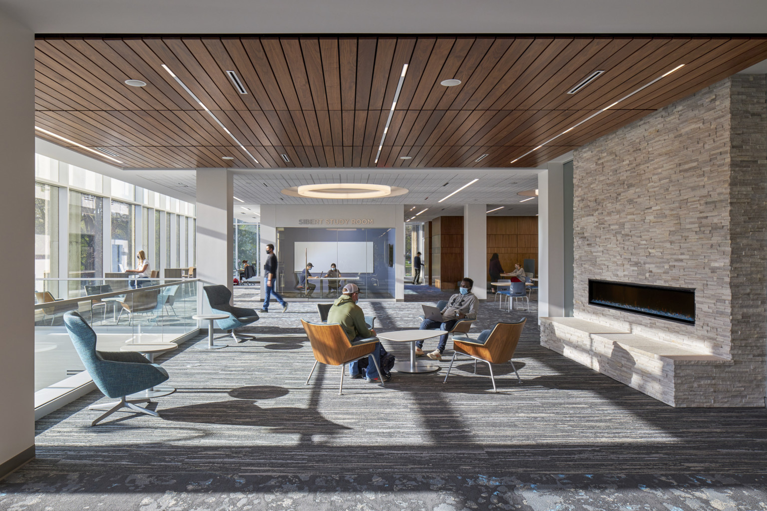 Seating area with tables and chairs next to fire place in room with wood panel ceiling with recessed lines of light