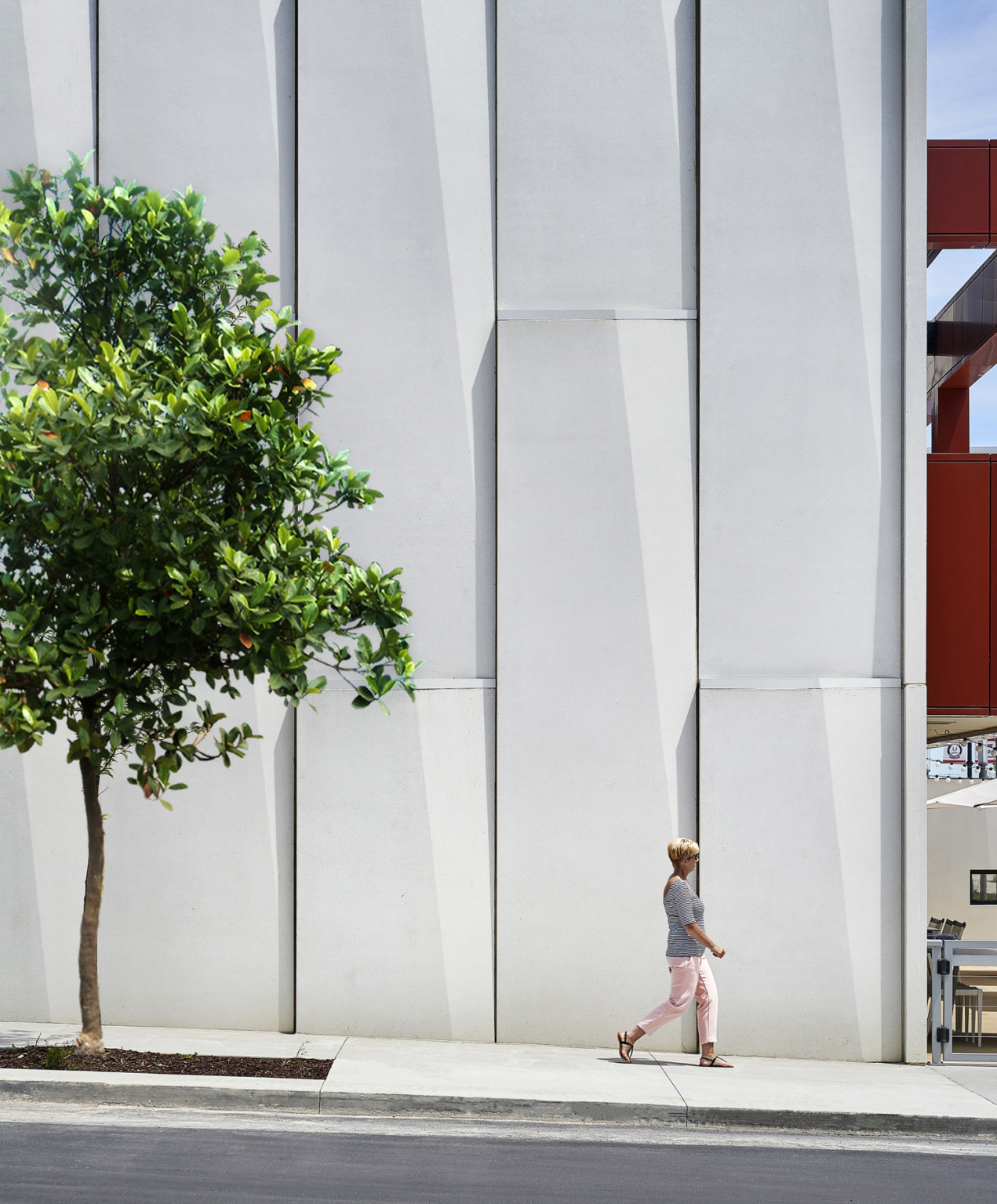 Textured white panels on exterior wall along treelined side walk