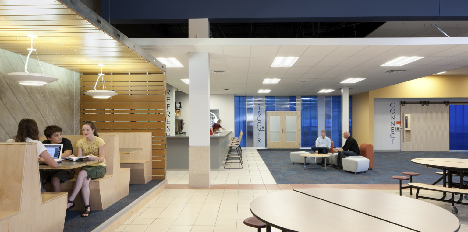 Wood wrapped ceiling over booths, left, in room with flexible seating. Blue shiny panels on back wall with word Discover