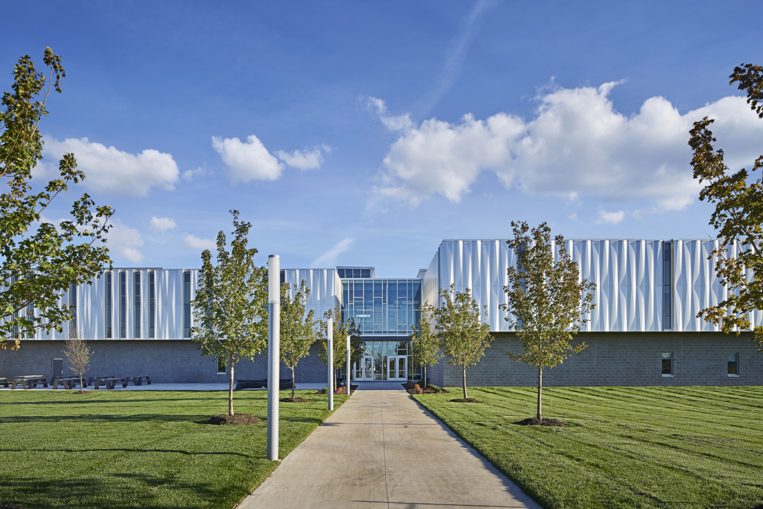 Front view of building looking down a treelined path to the front entrance with 2 sets of glass double doors