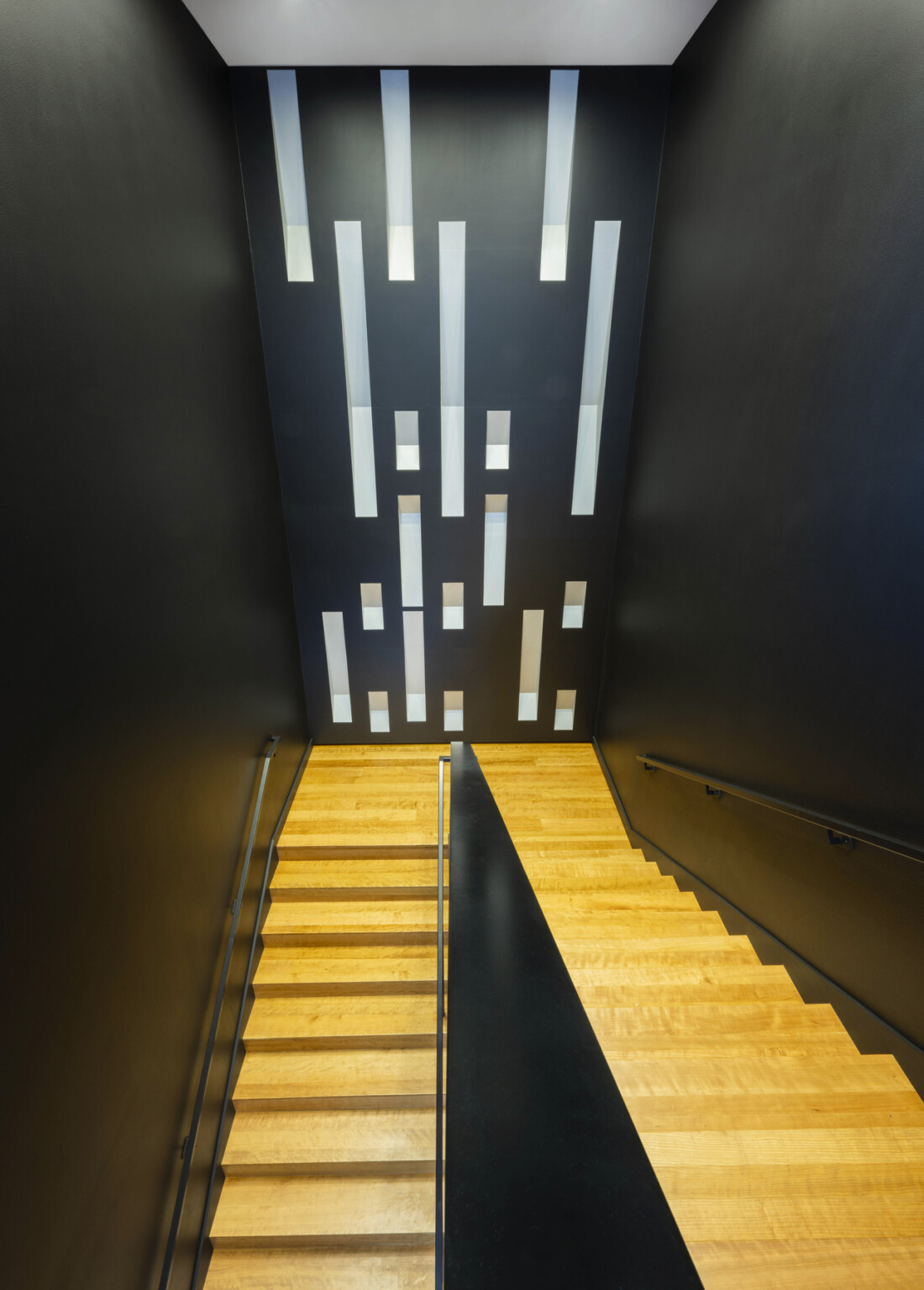 Interior yellow wood steps in black stairwell with pattern of long tin windows