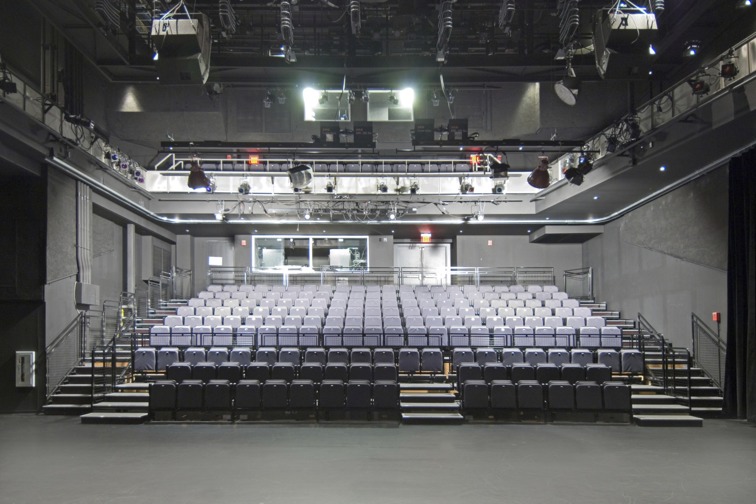 Two stories of stadium style grey seating in dark grey room with large light fixtures above