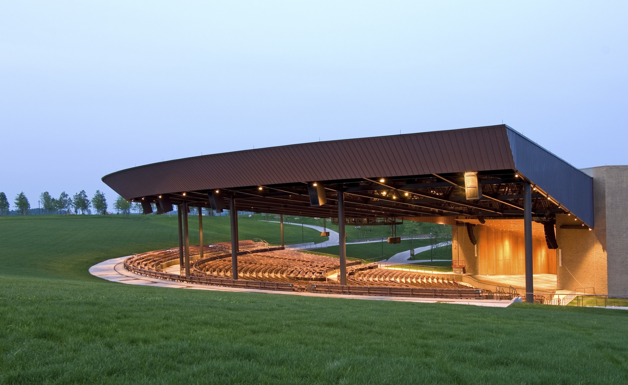 Bethel Woods Center for the Arts outdoor amphitheater illuminated with yellow light in the evening, amphitheater design, open air amphitheater; museum at bethel woods
