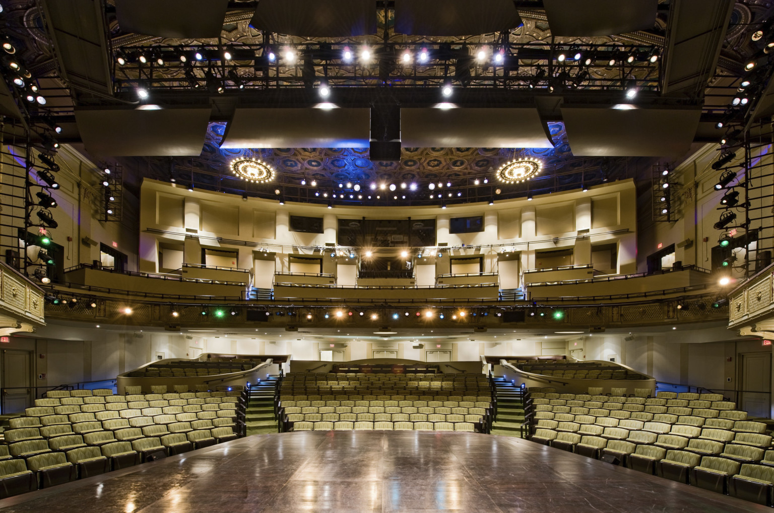 The Hanna Theater viewed from stage looking towards yellow patterned theater seats and balcony. Lighting systems frames stage