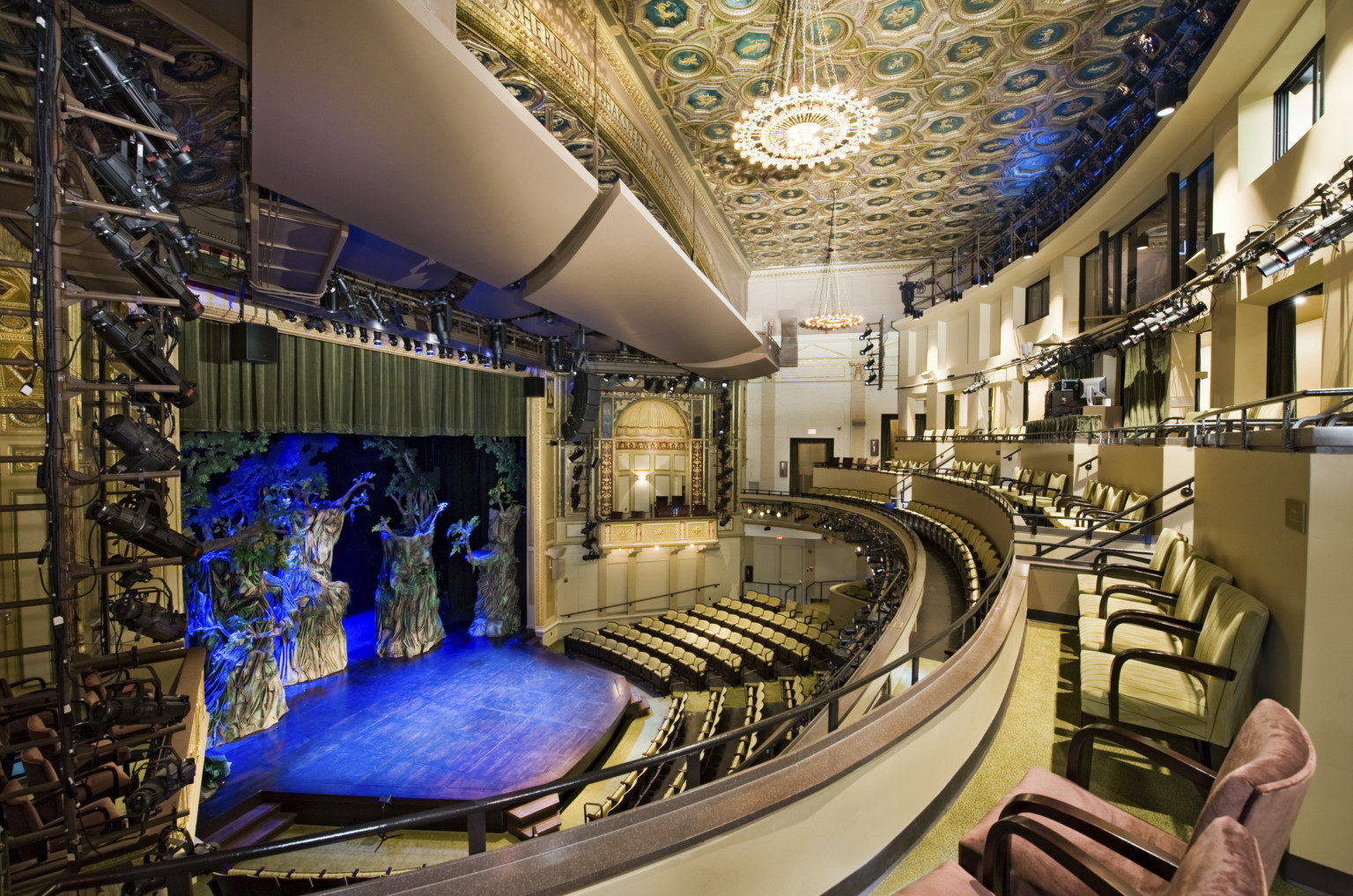 Multiple balconies in a theater with yellow seats and dark details, box seat center with arch overhang and gold details Multiple balconies in a theater with yellow seats and dark details, box seat center with arch overhang and gold details