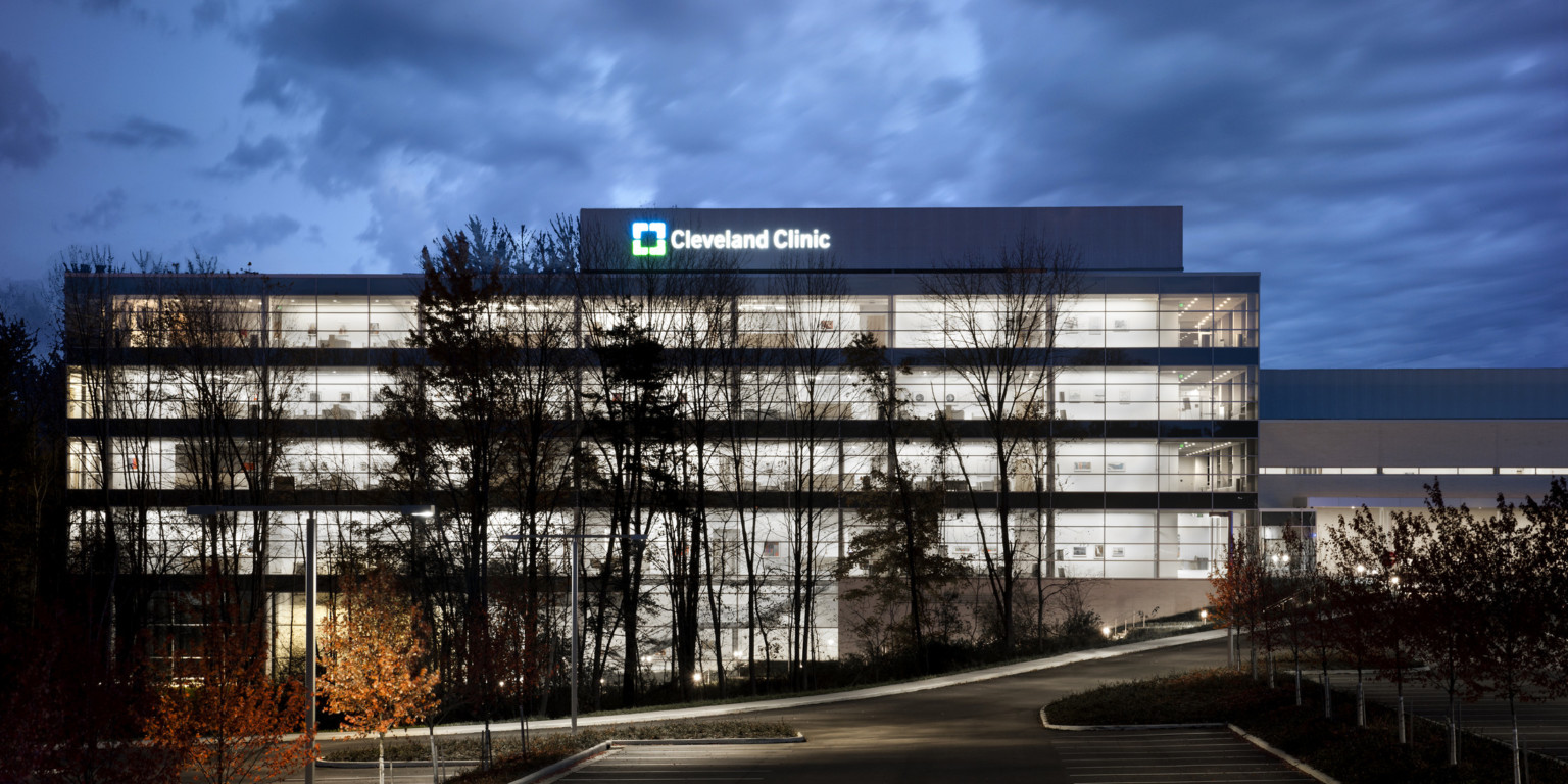 Exterior view of building illuminated at night with bottom floor built into hill. Lit sign at top reads Cleveland Clinic Exterior view of building illuminated at night with bottom floor built into hill. Lit sign at top reads Cleveland Clinic