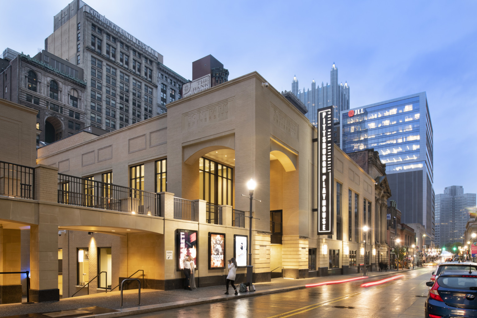 Exterior view of tan building with black illuminated Pittsburgh Playhouse sign, below ground entry and second floor walkway