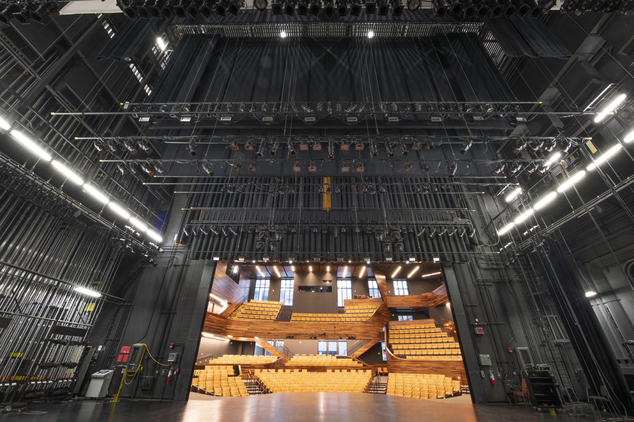 Looking from backstage outwards to dark colored stage rigging system hidden from yellow empty audience seats