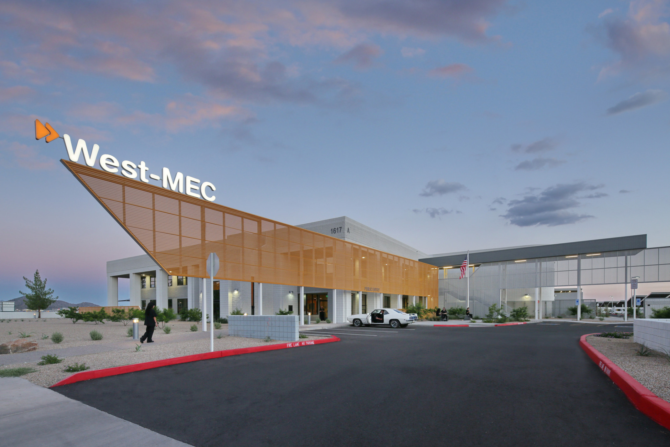 West-MEC Northeast Campus entrance with illuminated sign on top of orange perforated sunscreen extending past entrance
