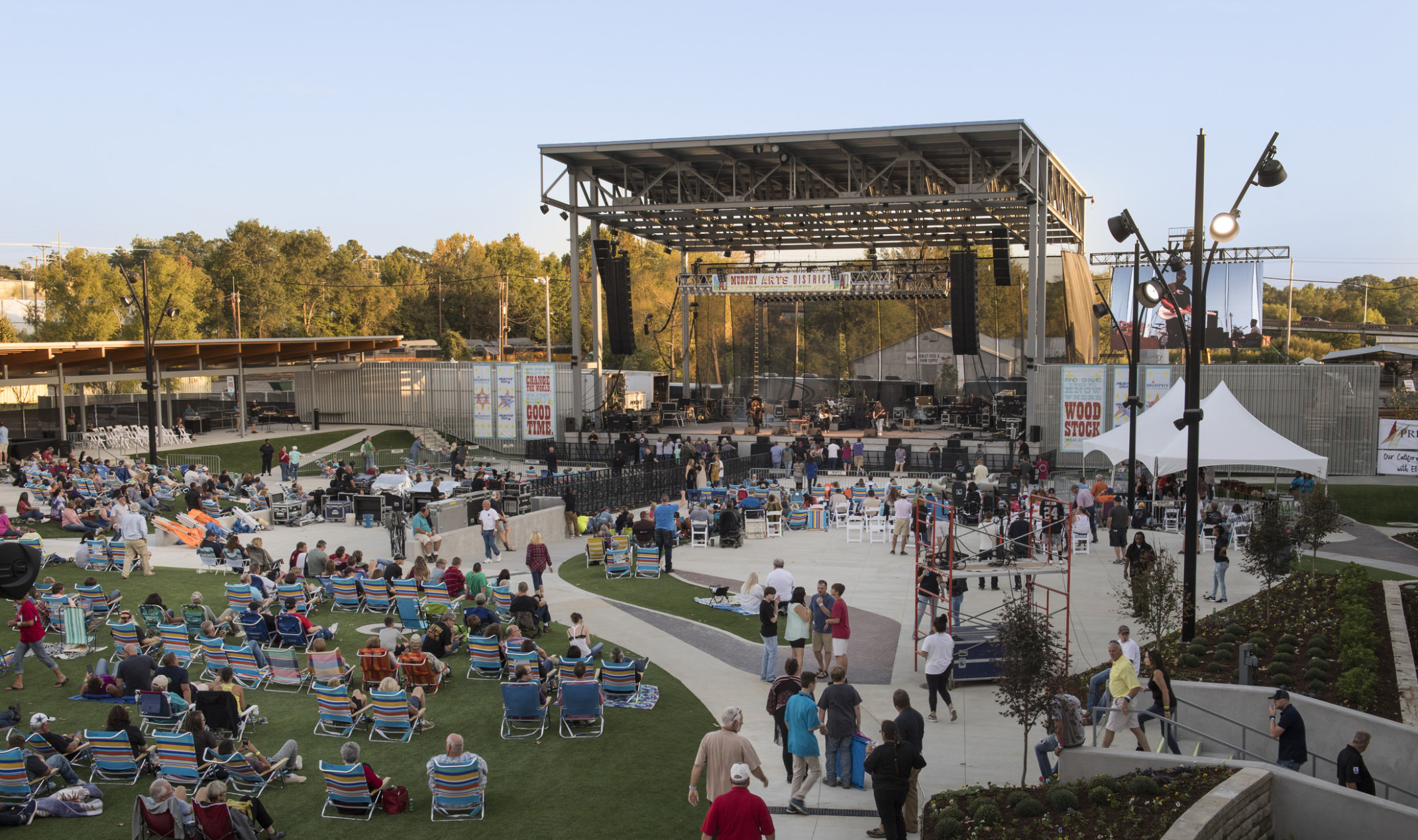 Crowd sitting in lawn chairs on grass and concrete facing outdoor stage