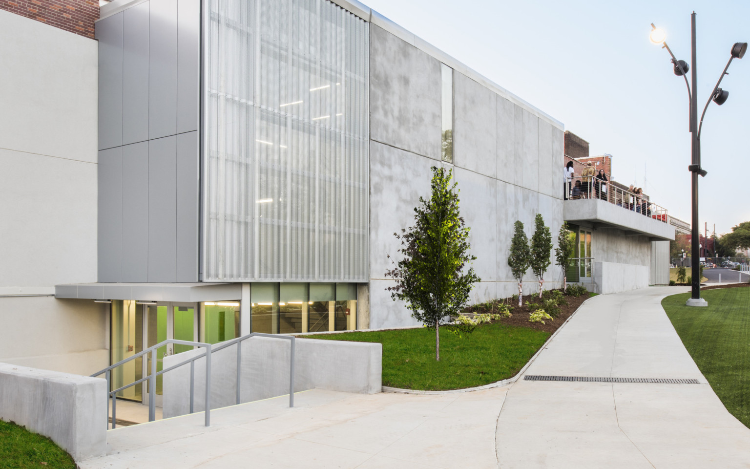 Corner view from sidewalk of glass and concrete building with people on second floor balcony at back