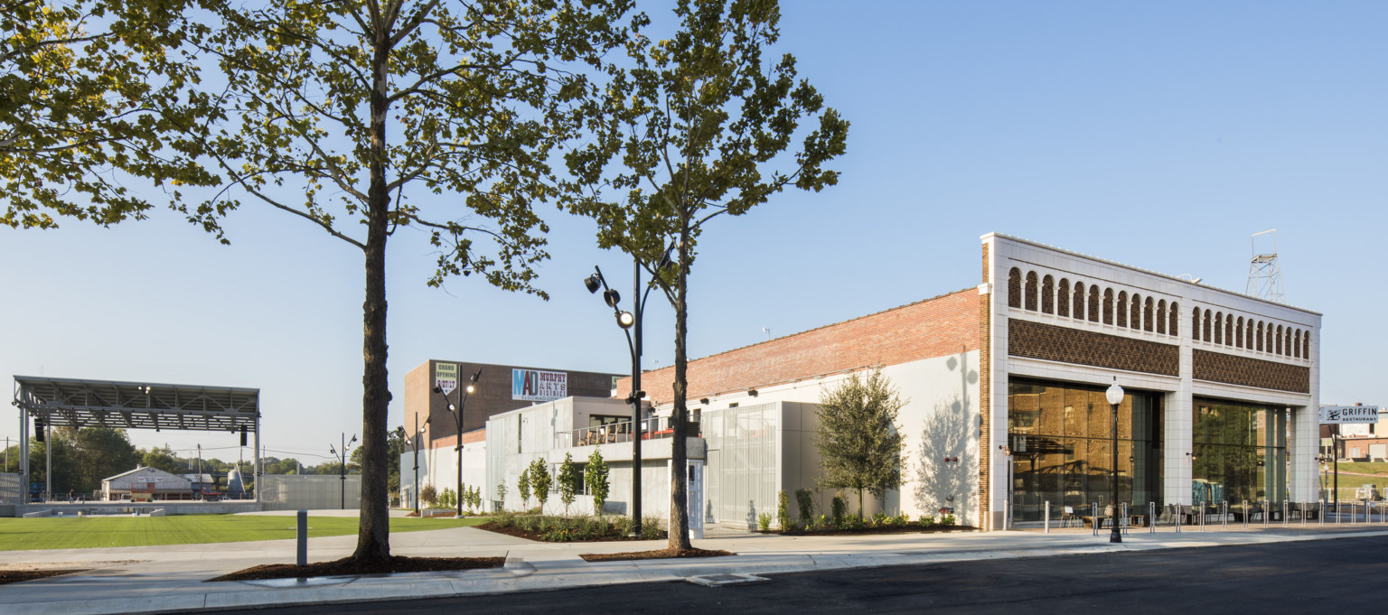 Corner view of brick building with white molded facade next to green field with pavilion roof