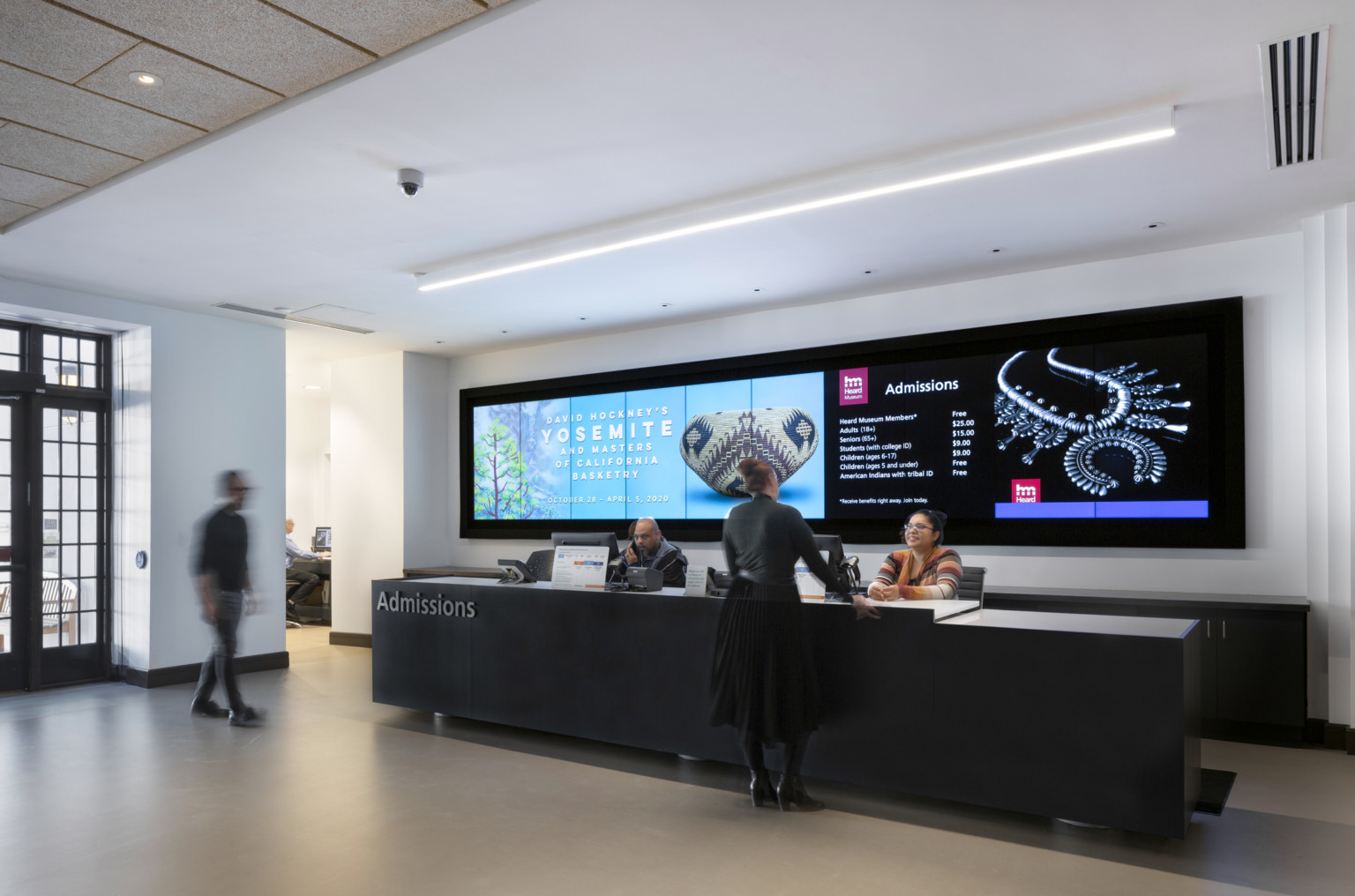 A large black admissions desk with a screen behind listing admission prices and exhibition announcements, interactive museum