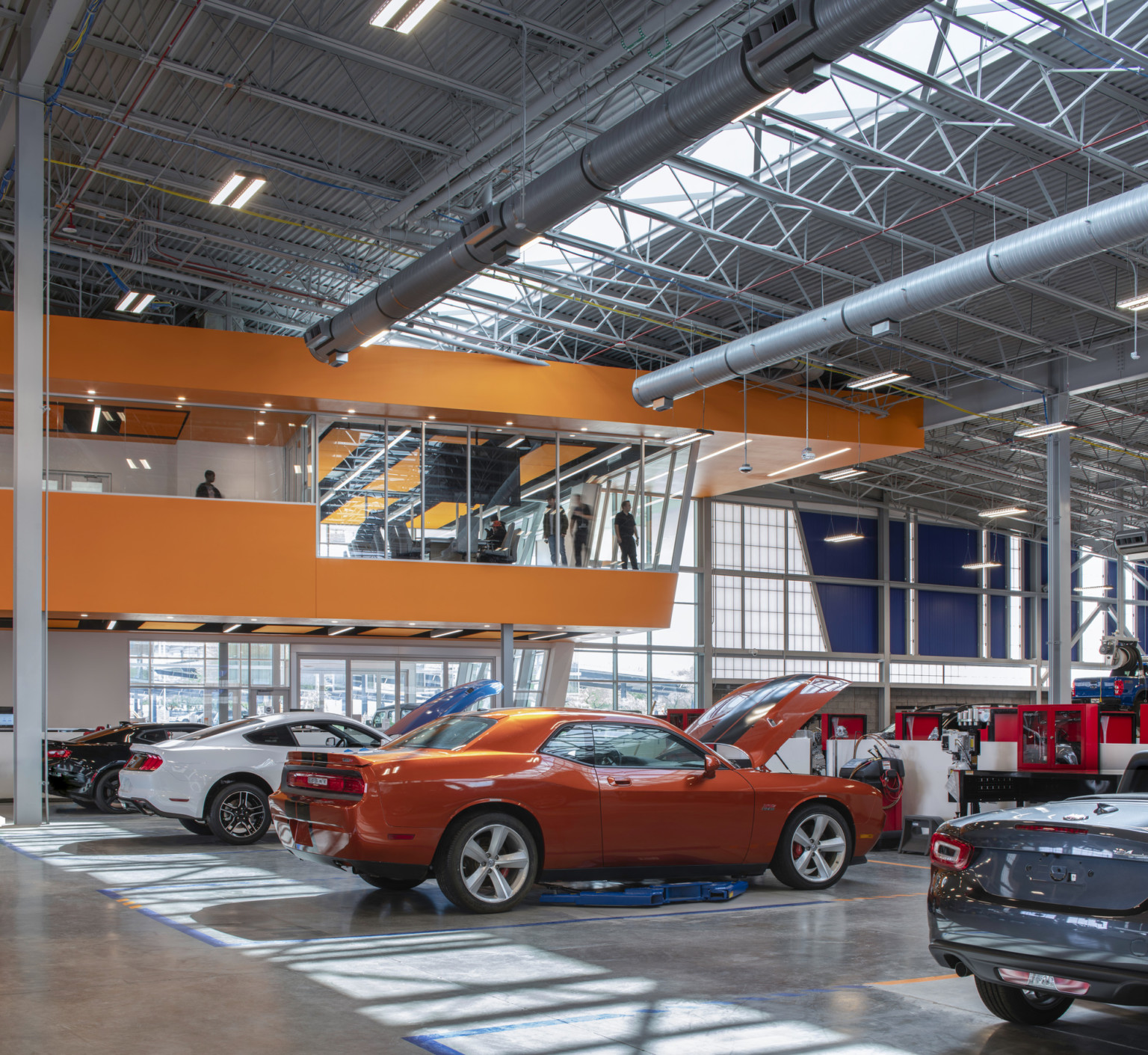 Glass room with Orange car under glass bannister to exposed second floor. Orange detail left