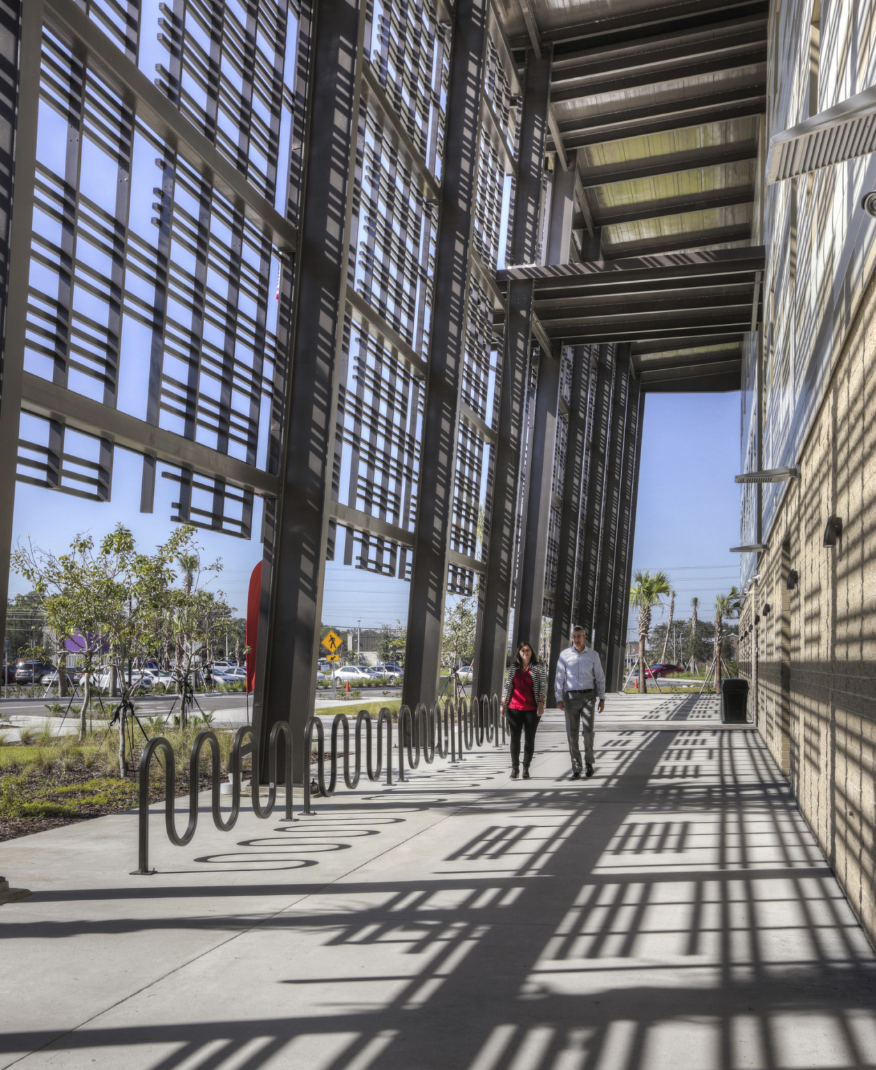 Walkway along perimeter of building. Bike racks right below geometric wrap on upper levels of building creating shadow design