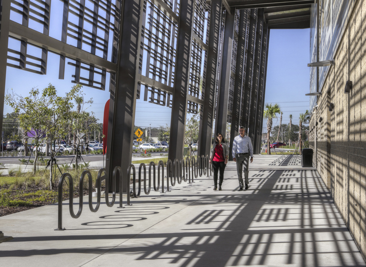 Walkway along perimeter of building. Bike racks right below geometric wrap on upper levels of building creating shadow design