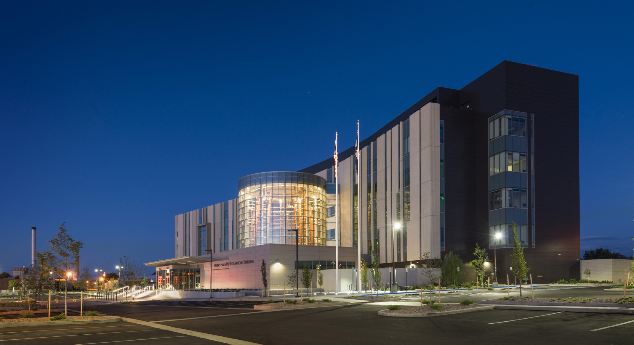 The Dennis Maes Pueblo Judicial Building illuminated at night from the glass cylindrical tower at center above the entry
