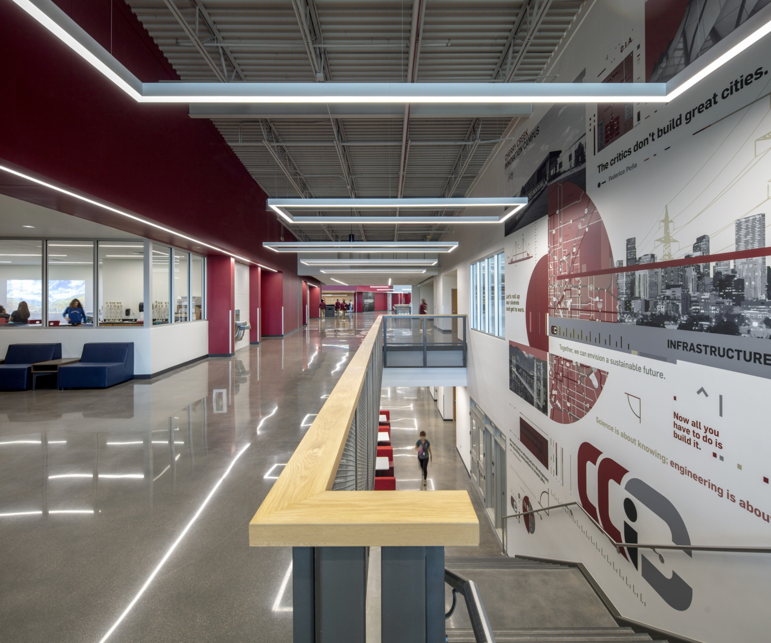 Mural on right wall next to stairs to 2nd floor. Red wall to left with white recession with seating by classroom windows