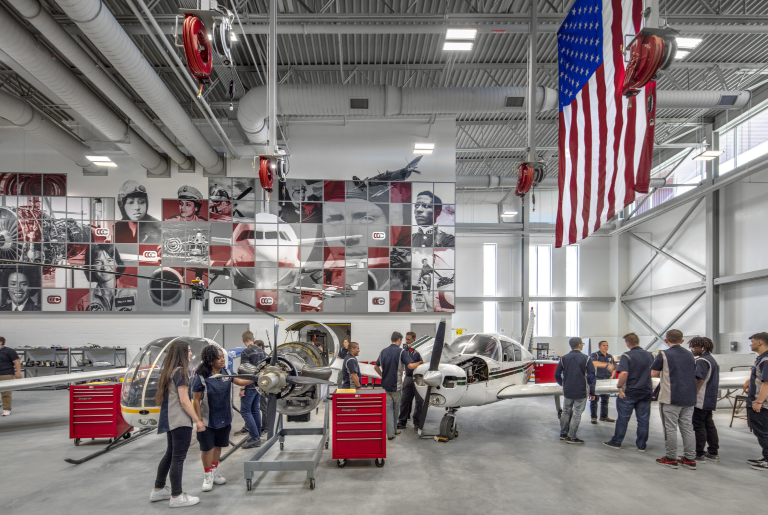 Aviation lab with helicopter, small plane, and displayed engine, mural at back with planes and pilots, american flag, right