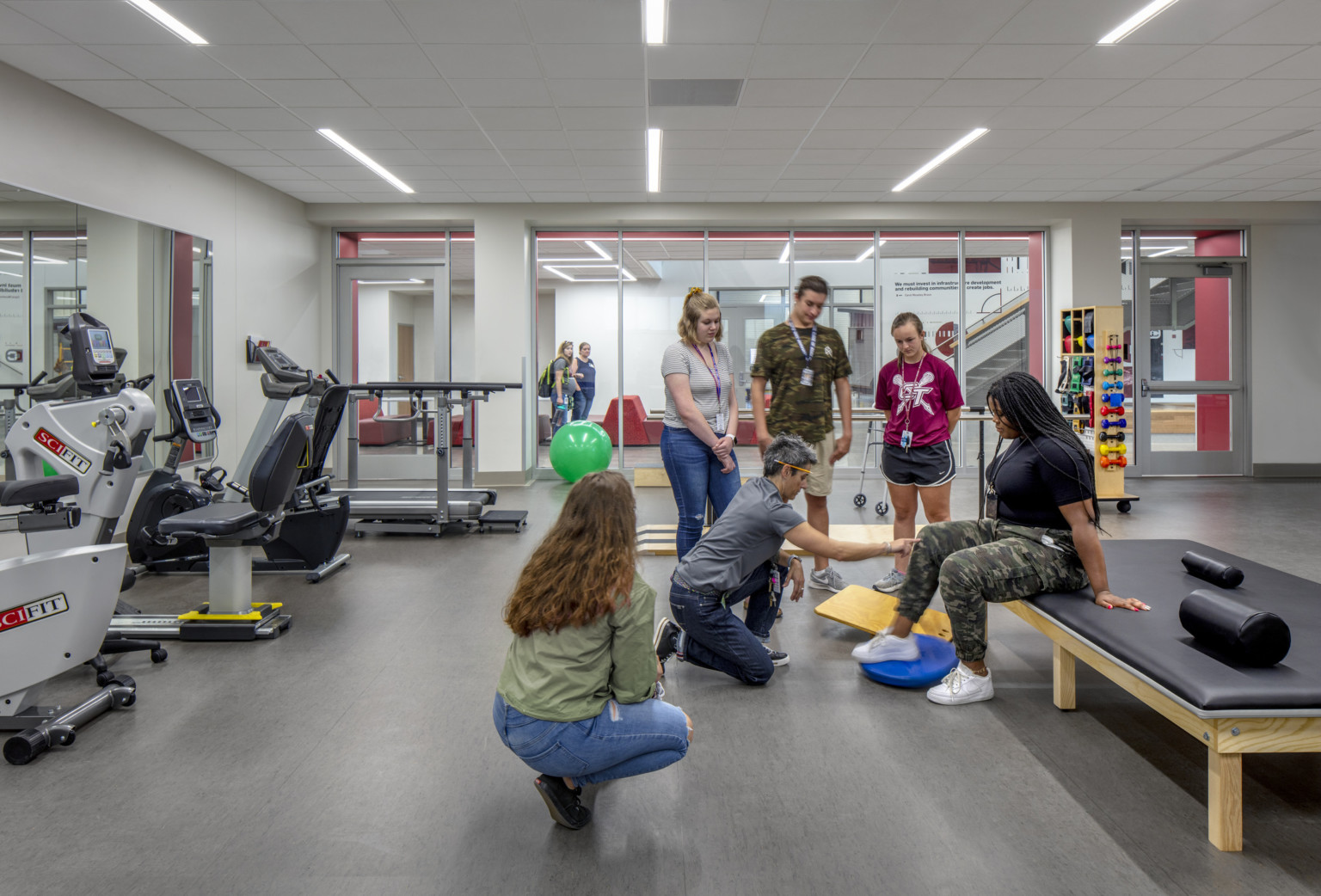 Classroom with cardio equipment to left wall facing mirror. Floor to ceiling windows, back, to hallway. Padded bench, center