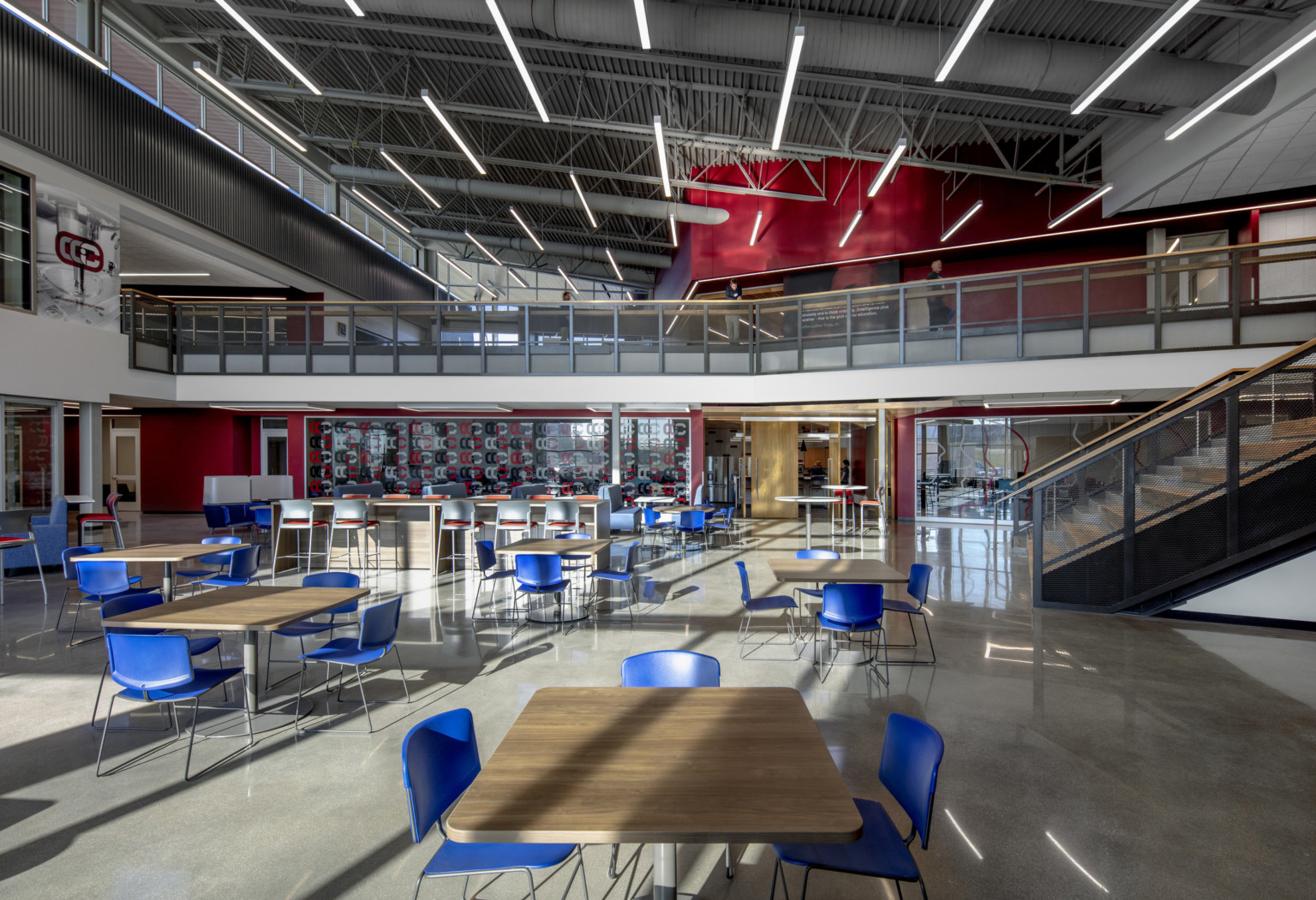 Seating area in double height room with natural lighting. 2nd floor walkway to back extends over entrance to classroom