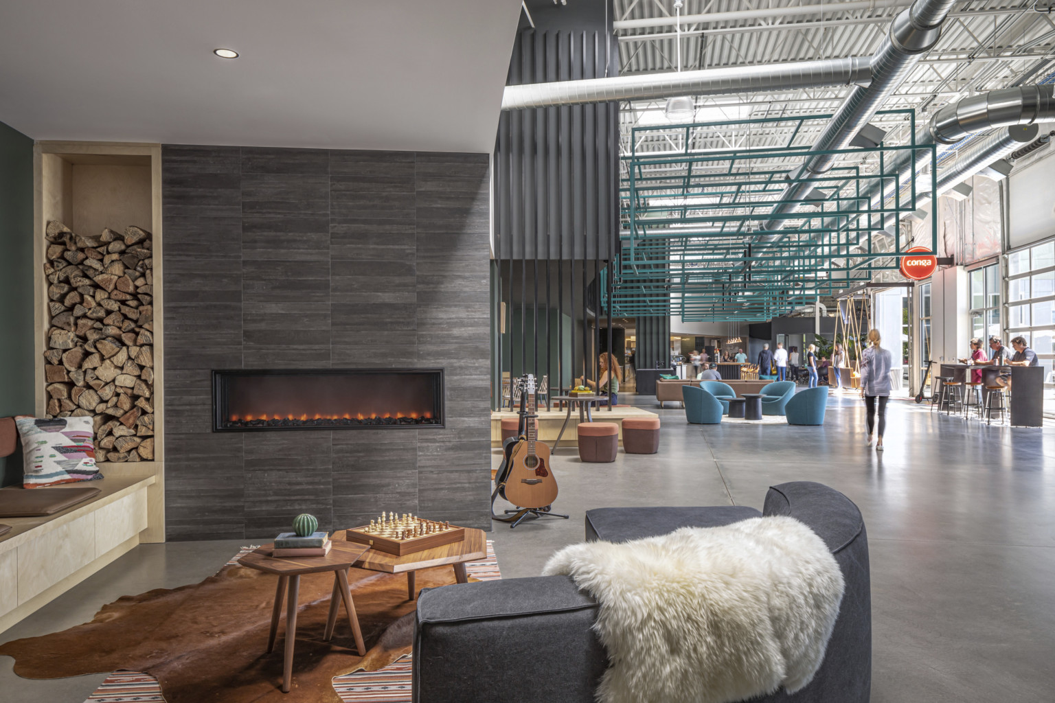 Conga Headquarters seating area with garage door windows on right wall. Couch at front left in front of fireplace