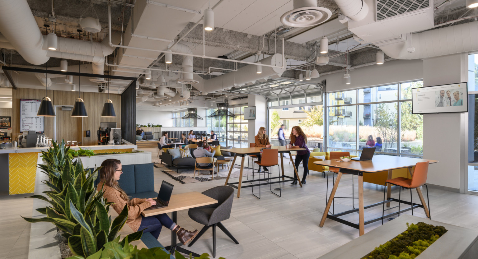 Mixed seating with tables in room with floor to ceiling windows with open garage style door, right. Coffee counter to left