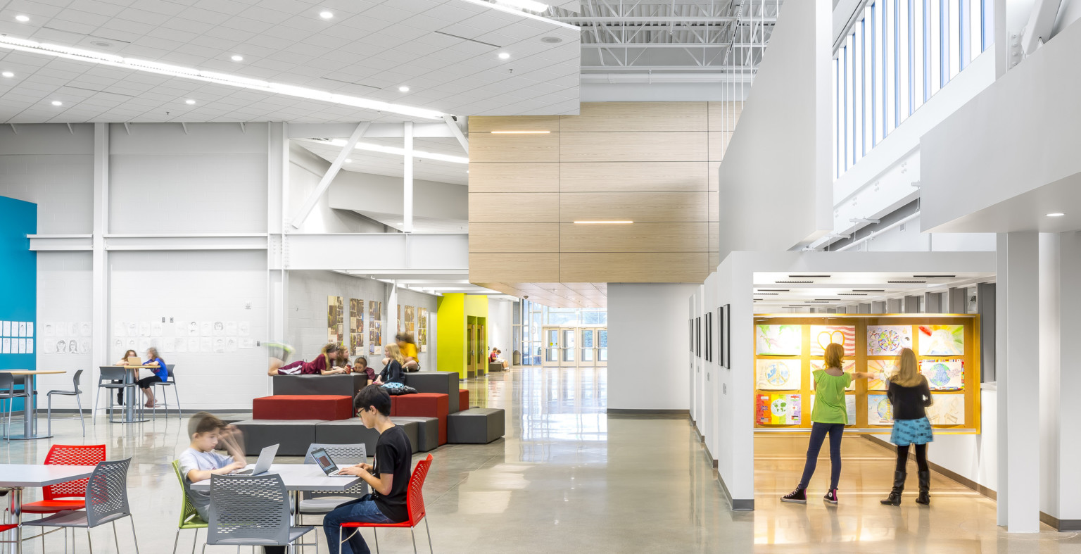 A white room with exposed structural beams. Ergonomic seating. Right, an atrium with art displayed. Wood drop ceiling detail