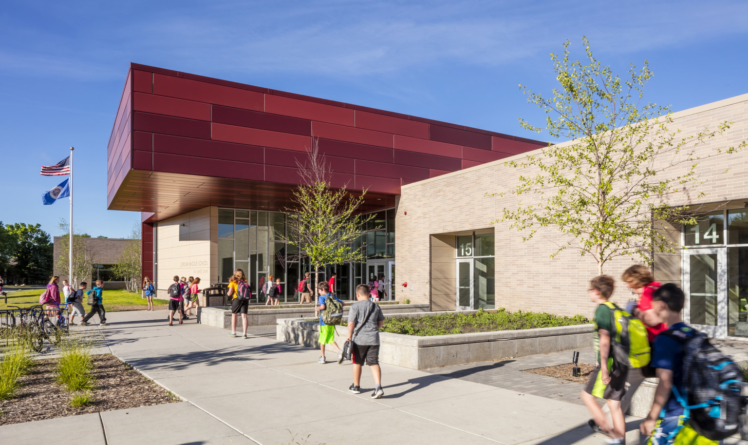 Jordan Middle School exterior entrance with floor to ceiling windows around doors, beige brick walls, and a dark red overhang