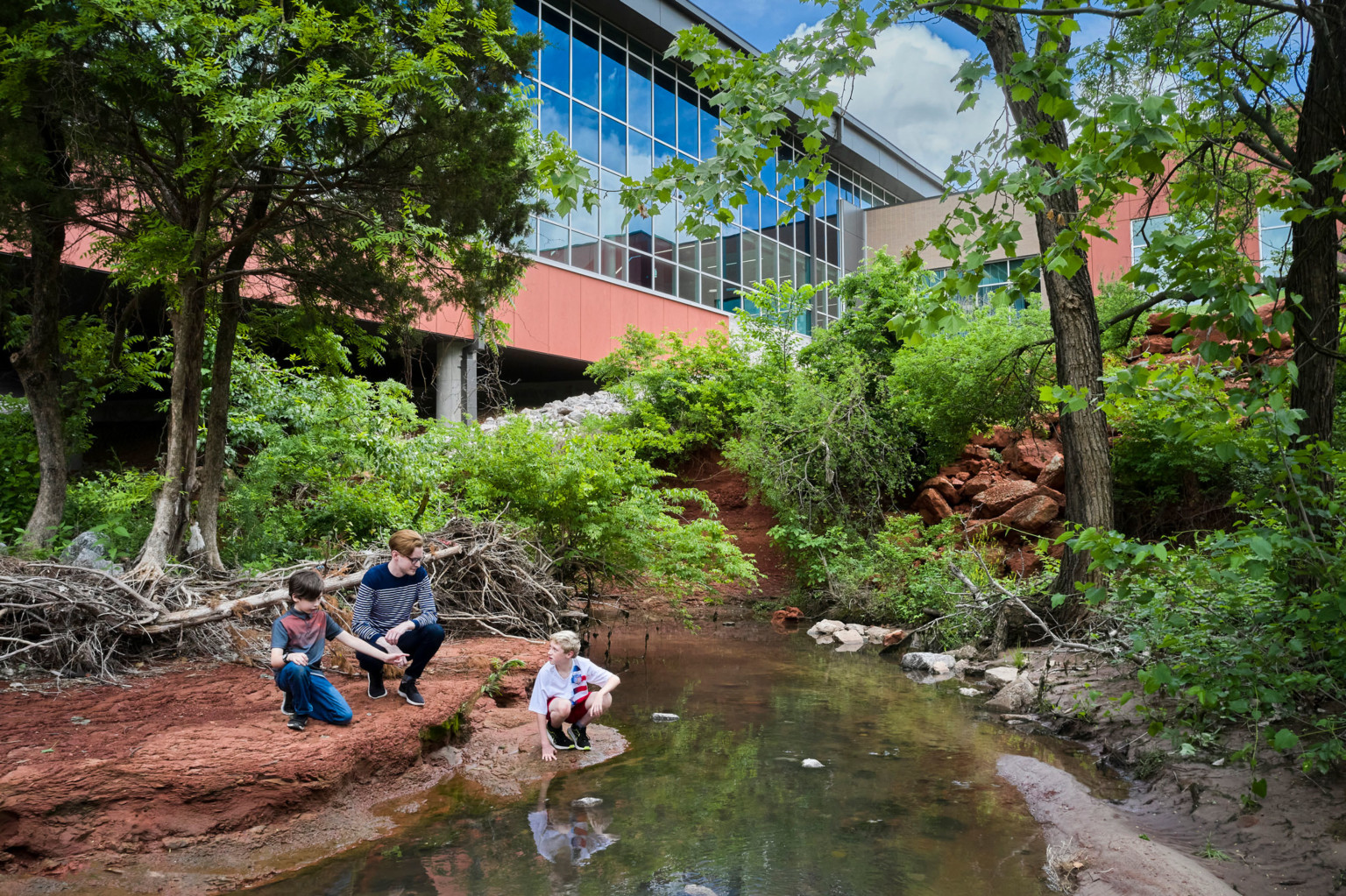 Small creek surrounded by wooded area beside the windowed hallway