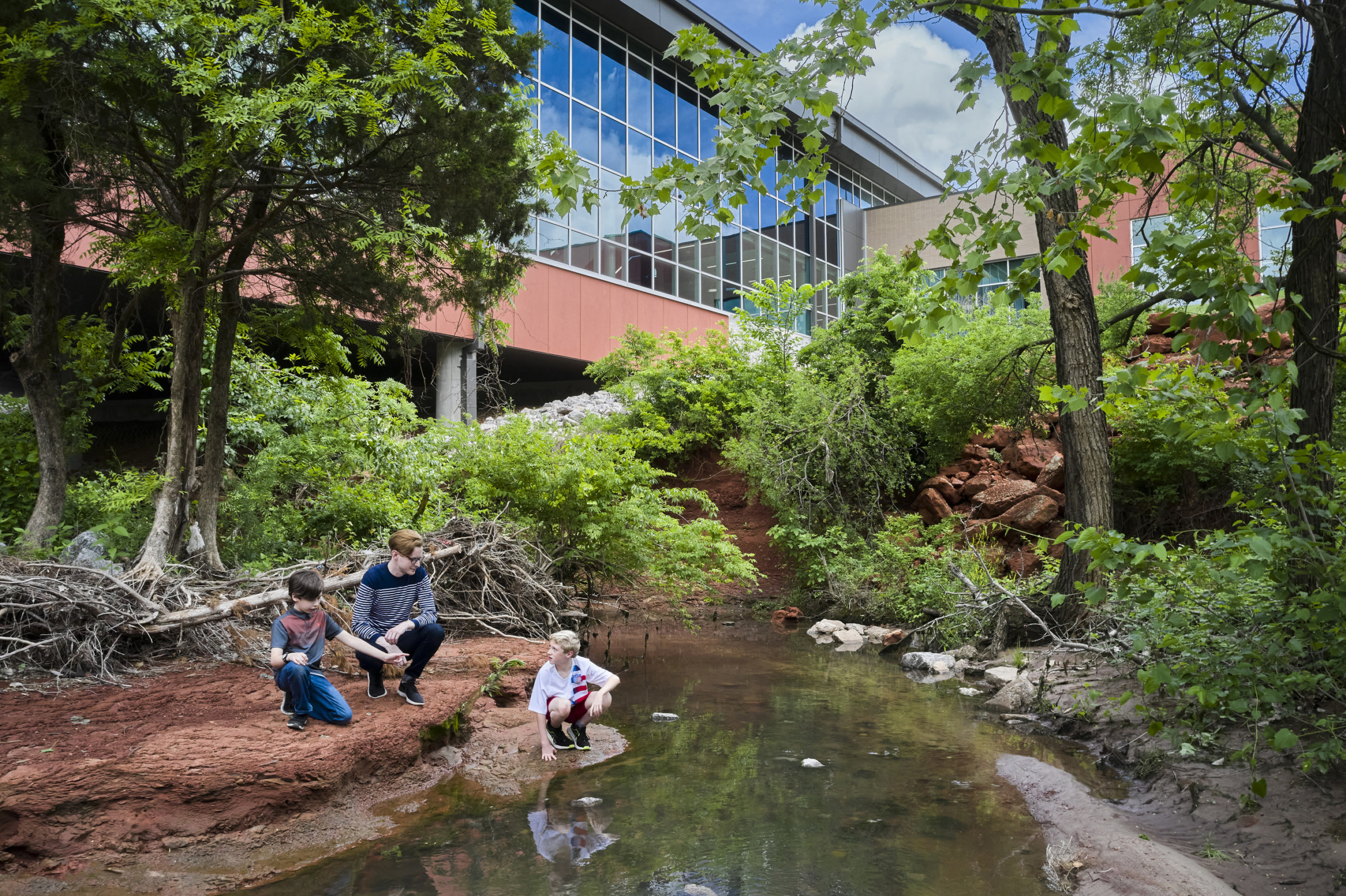 Small creek surrounded by wooded area beside the windowed hallway