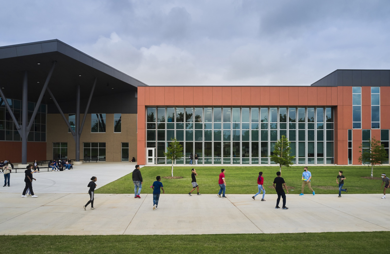 James L. Capps Middle School exterior with angled black shelter brick building. Orange wrap facade over double height glass