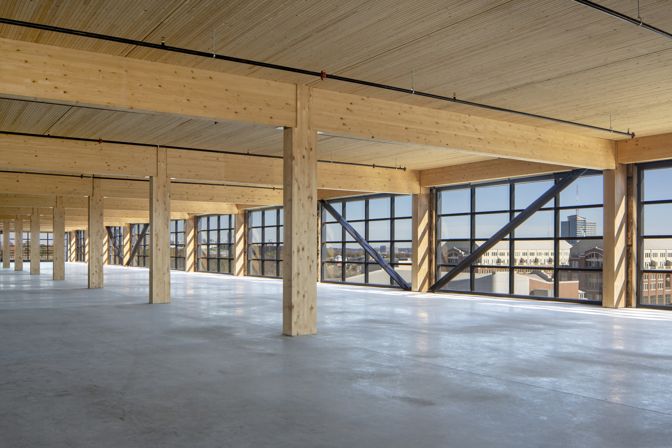 Interior with wood columns, ceiling and beams lined with floor to ceiling windows with black seams and exposed steel beams