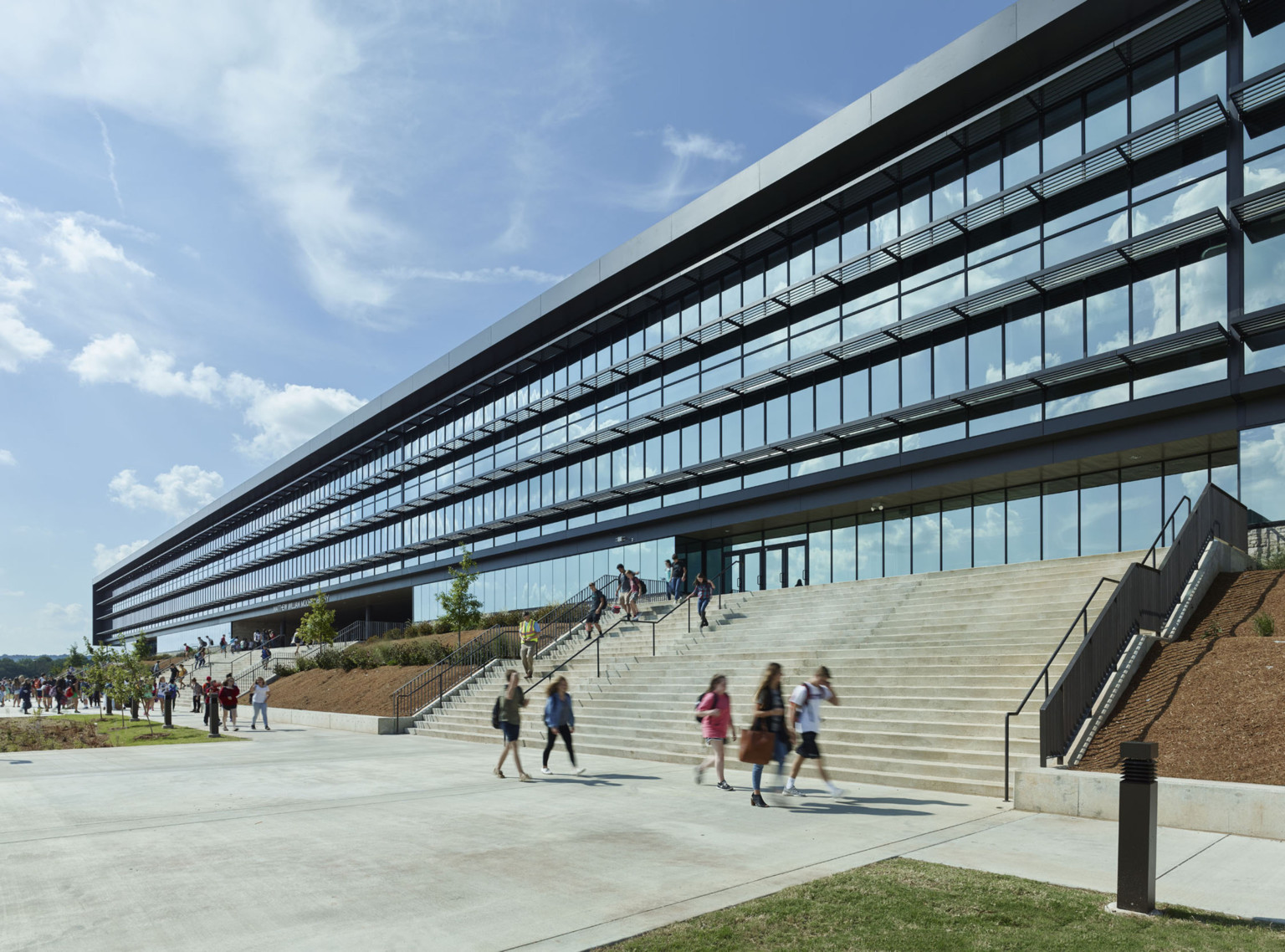 2 sets of wide concrete steps in front of floor to ceiling windows and glass entry doors. Steps separated by hill with trees