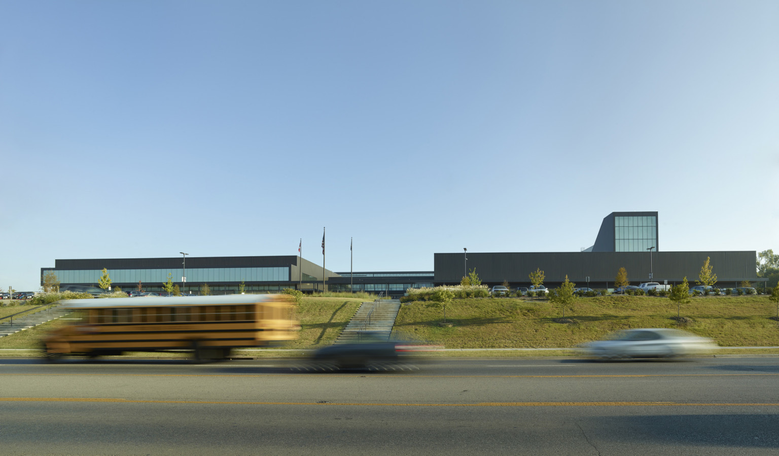 Exterior view of the school from across the street. Concrete steps are built into green hill leading up to the black building