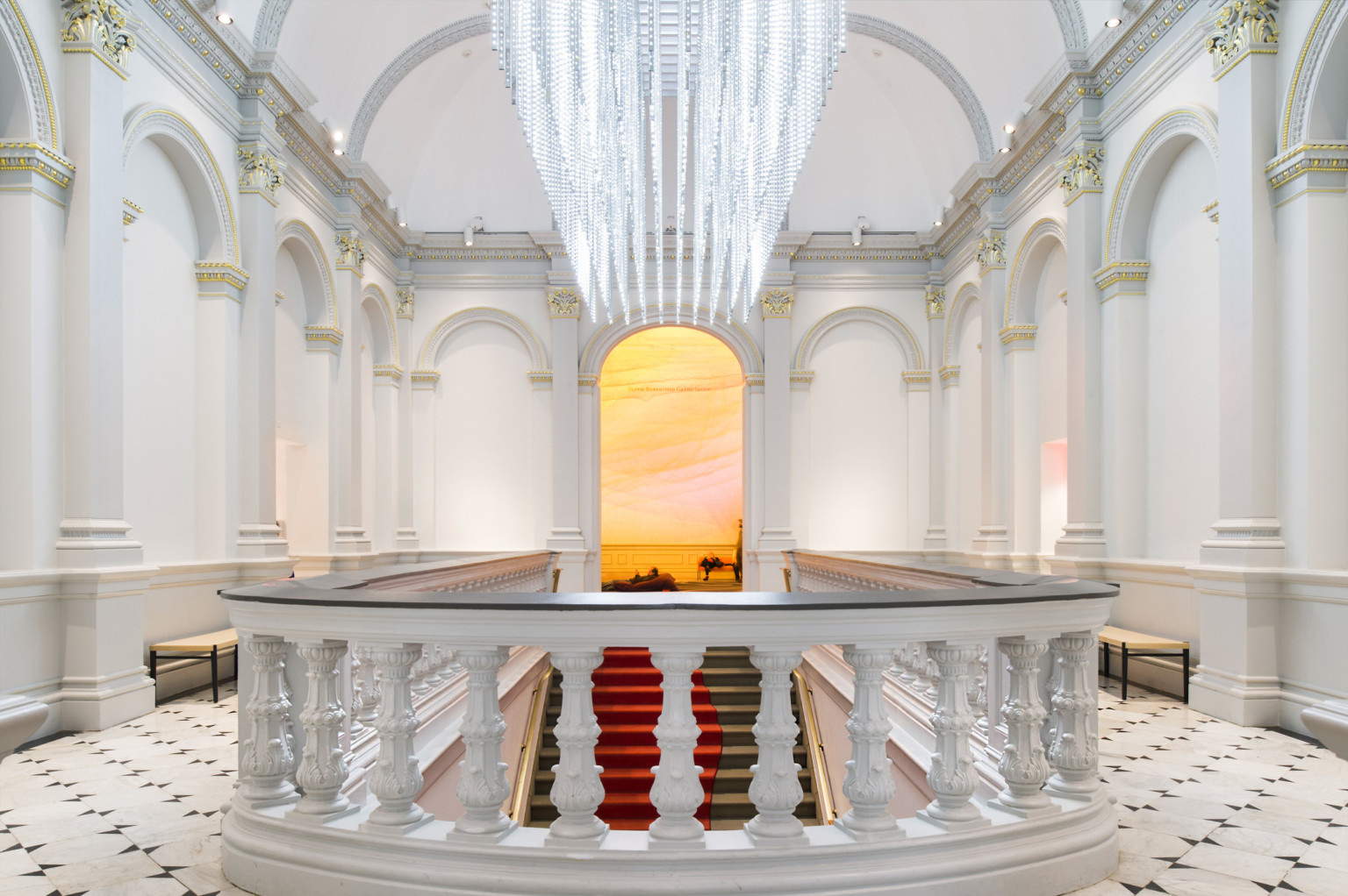 Custom sculptural chandelier hanging above staircase in white room at Renwick Gallery, banister with dark accent in front Custom sculptural chandelier hanging above staircase in white room at Renwick Gallery, banister with dark accent in front