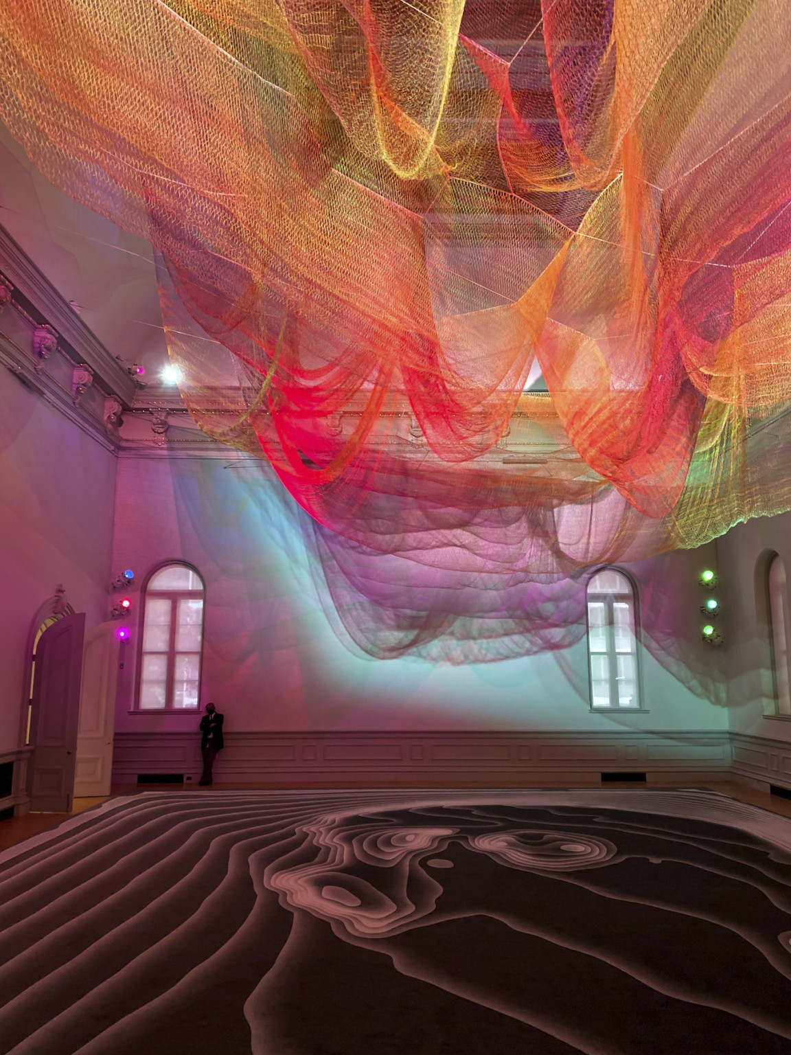 Colorful abstract art installation with red and orange light on layers of sheer netting with shadows and light on white wall Colorful abstract art installation with red and orange light on layers of sheer netting with shadows and light on white wall