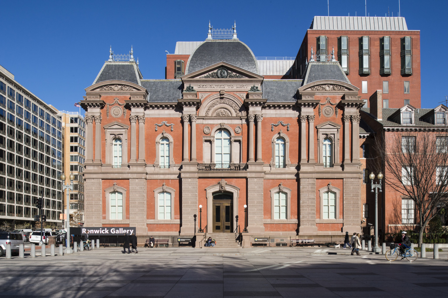 The front entrance to a two story red brick Second Empire style building with masonry and Dedicated to Art is carved at top